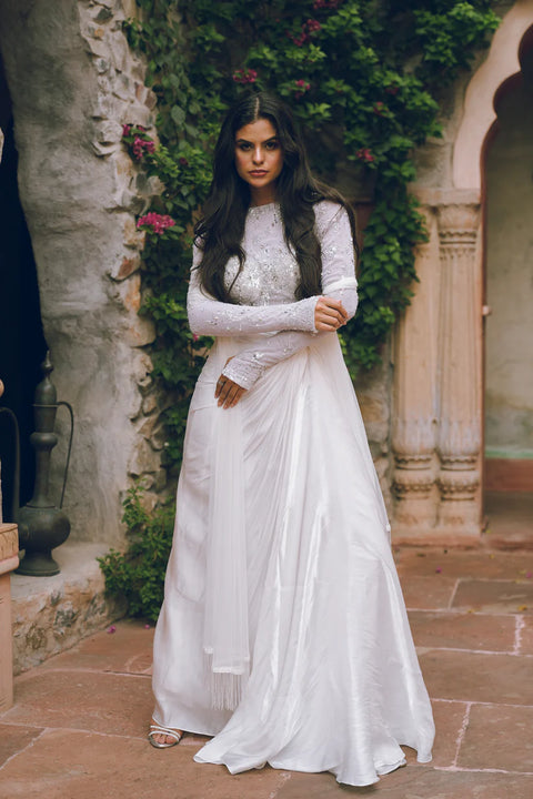 An ivory draped ensemble with a hand- embroidered corset bustier top and fluid silk drape. Subtle crystal accents add a refined shimmer, making it perfect for weddings, soirées, and modern celebrations.