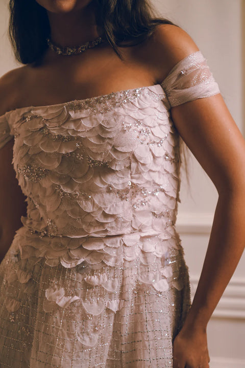 A lavender off-shoulder gown with floral appliqué and crystal detailing, flowing gracefully with timeless charm. Designed for soirées, weddings, and modern celebrations.