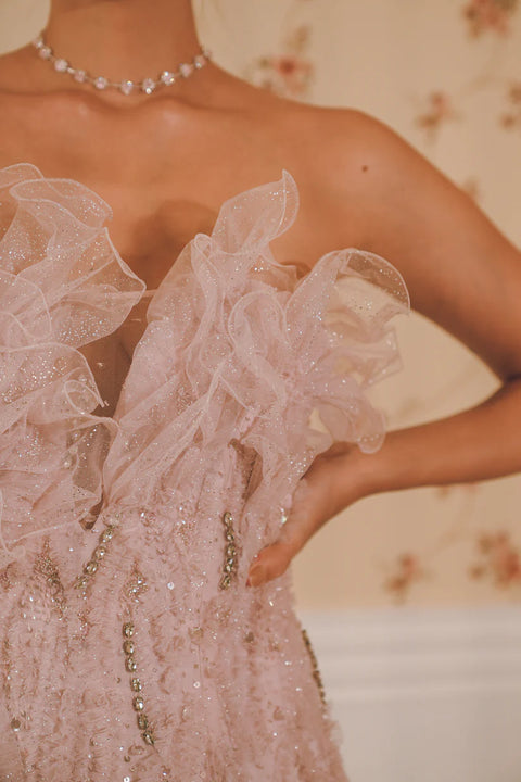 A lavender ruffled gown adorned with sequins, pearls, and crystal accents, layered in delicate tulle. Designed for fluid movement and radiant sparkle. Perfect for cocktail nights and statement celebrations.